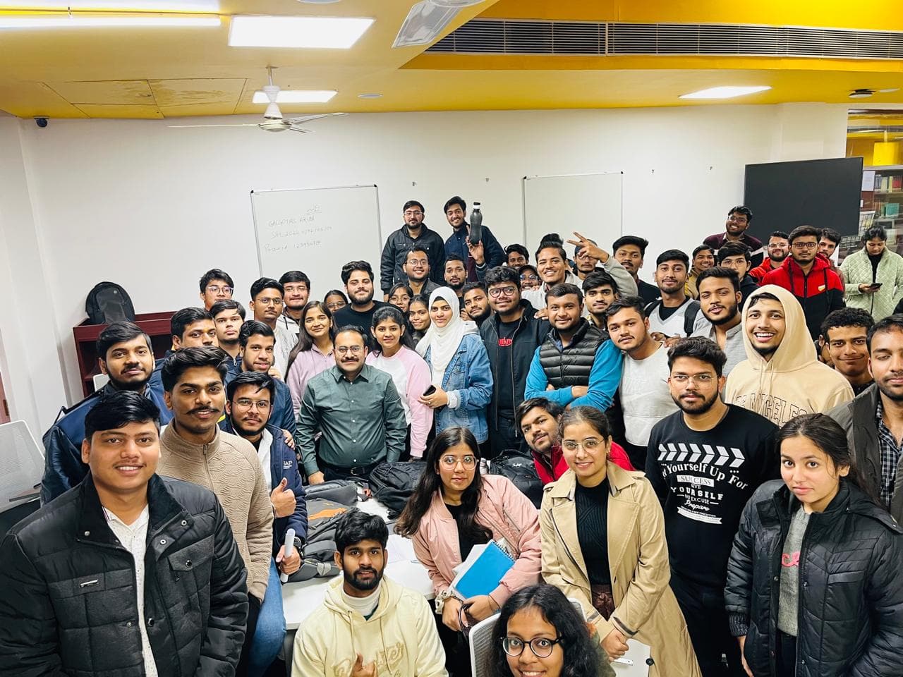 A large group of students and their mentor posing together in a classroom